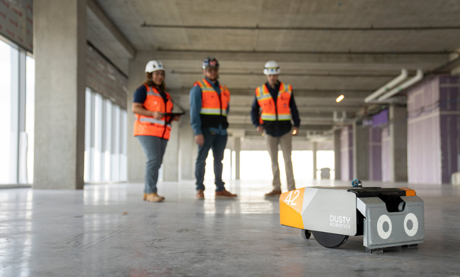 3 Swinerton employees holding remote that is driving the robot named Dusty